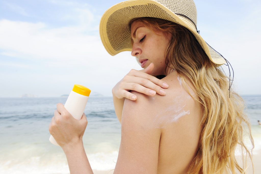 woman applying suntan lotion at the beach smiling