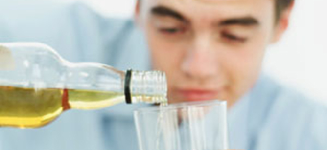 close-up of a teenage boy pouring wine from a bottle into a glass